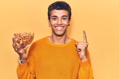 Elinde simit tutan genç Afrikalı Amerikalı bir adam bir fikir veya soruyla gülümsüyor ve mutlu bir yüzle işaret ediyor. 
