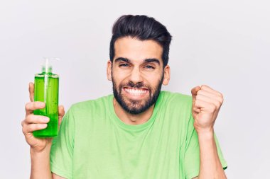 Sakallı genç yakışıklı adam aloe vera kremi şişesi giymiş gururla bağırıyor zaferi ve başarıyı kutluyor. 
