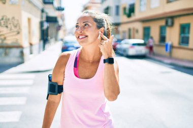 Orta yaşlı sporcu kadın gülerek antrenman yapıyor ve şehirde kulaklık takıyor.