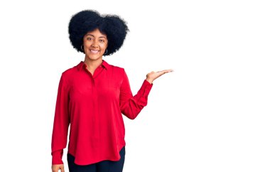 Genç Afro-Amerikan kızı günlük giysiler giymiş neşeli bir şekilde gülümsüyor ve avuç içiyle kameraya bakıyor.. 