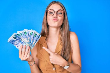 Genç sarışın kız elinde Güney Afrika rand banknotları tutarken kameraya bakıyor ve öpüşüp koklaşıyor ve seksi oluyor. aşk ifadesi. 