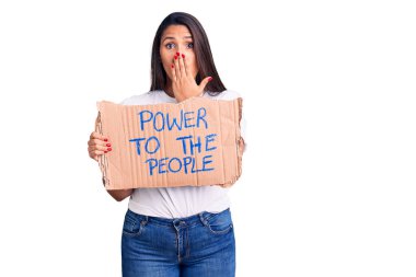 Genç ve güzel bir kadın karton pankartlara güç veriyor. Ağzı eliyle kapatıyor. Şok geçiriyor ve hata yapmaktan korkuyor. şaşırmış ifade 