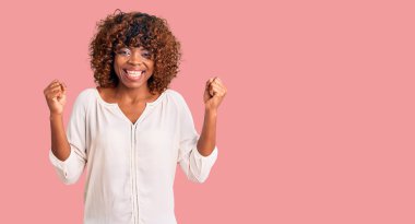 Genç Afrikalı Amerikalı kadın gündelik giysiler içinde gururla bağırıyor, zaferi kutluyor ve kollarını kaldırarak heyecanlanıyor. 