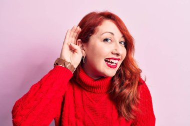 Genç, güzel, kızıl saçlı bir kadın pembe arka planda kırmızı balıkçı yaka kazak giyip, sırıtarak dedikodu ya da dedikoduları dinliyor. Sağırlık kavramı.