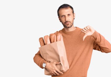 Elinde kızgın yüzlü ekmek torbası olan genç yakışıklı bir adam, olumsuz işaret baş parmakları aşağıda, reddedilme konsepti. 
