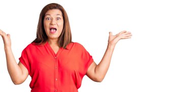 Orta yaşlı Latin kadın gündelik kıyafetler giyip zaferi mutlu bir gülümsemeyle kutluyor ve kazanan yüz ifadesi kaldırıyor. 