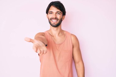 Yakışıklı, sıradan kıyafetler giyen, samimi bir şekilde gülümseyen, selamlaşmak ve selamlamak için elini sıkan bir İspanyol. başarılı iş. 