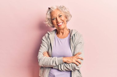 Son sınıf gri saçlı, sıradan spor kıyafetler giyen mutlu yüzlü, kollarını kavuşturup kameraya bakan bir kadın. pozitif kişi. 