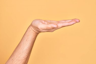 Beyaz bir gencin eli, izole edilmiş sarı arka plan üzerinde parmaklarını gösteriyor. Düz palmiye ürünü sunuyor, el hareketi yapıyor, boş kopya alanı veriyor.