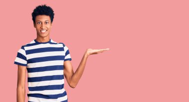 Genç Afrikalı Amerikalı sıradan kıyafetler giymiş neşeli bir şekilde gülümseyen ve avuç içi kameraya bakan biri.. 