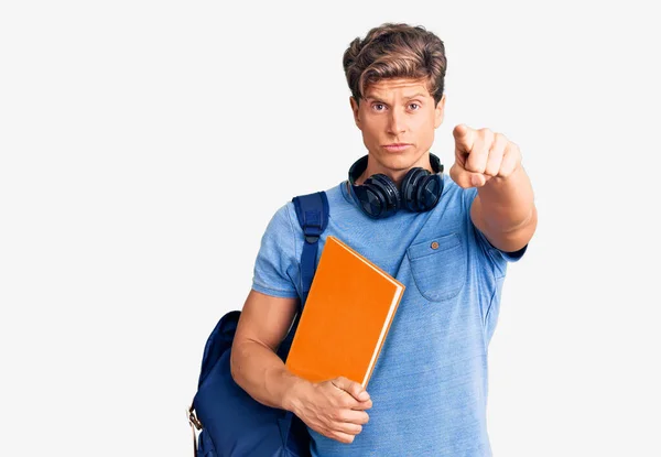 Joven Hombre Guapo Con Mochila Estudiante Auriculares Sosteniendo Libro Apuntando —  Fotos de Stock