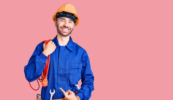 Jovem Hispânico Vestindo Uniforme Eletricista Segurando Cabo Sorrindo Feliz Apontando — Fotografia de Stock
