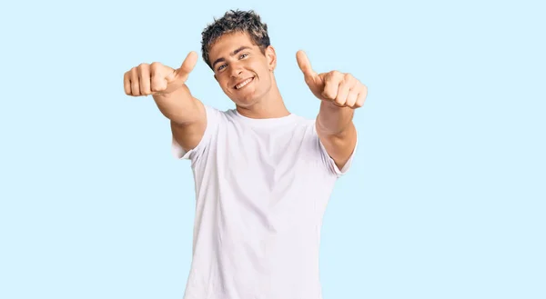 年轻英俊的男人穿着随意的白色T恤 肯定用手做积极的手势 微笑着竖起大拇指 为成功感到高兴 优胜手势 — 图库照片