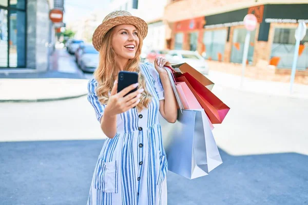 아름다운 점원이 웃으며 쇼핑백을 가게에 행복하게 갑니다 스마트폰을 사용하여 행복하게 — 스톡 사진