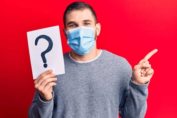 Ung Stilig Man Bär Medicinsk Mask Håller Frågetecken Ler Glad — Stockfoto