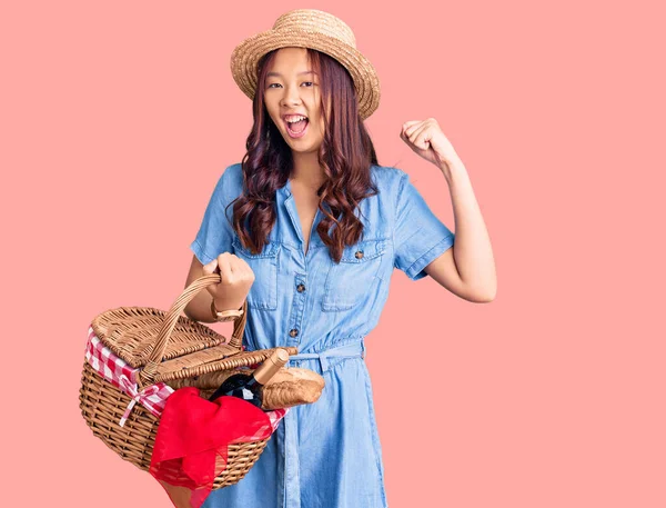 年轻美丽的中国姑娘戴着夏帽 带着面包的野餐柳条篮 自豪地尖叫着 高举双臂庆祝胜利和成功 — 图库照片