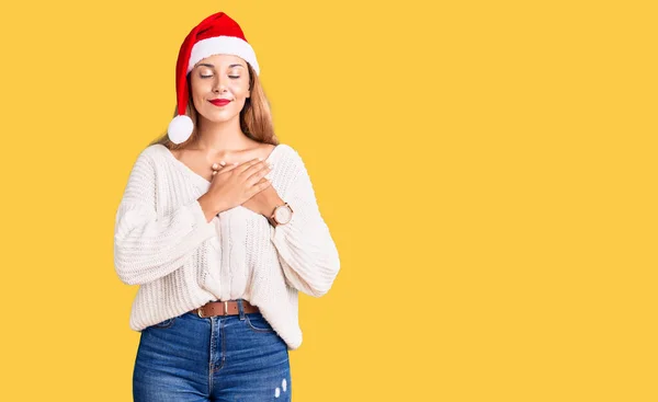Красивая Молодая Женщина Рождественской Шляпе Улыбаясь Руками Груди Закрытыми Глазами — стоковое фото
