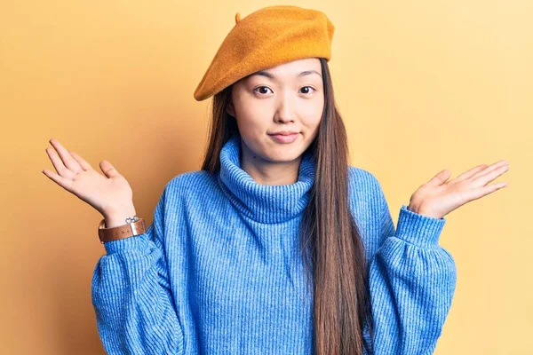 年轻美丽的中国女人 身穿高领毛衣 头戴法式贝雷帽 毫无头绪 与张开的双臂混淆不清 毫无头绪 满脸疑惑 — 图库照片