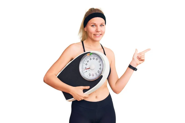 Spor Kıyafetleri Giyen Genç Sarışın Bir Kadın Tartı Makinesi Tutuyor — Stok fotoğraf