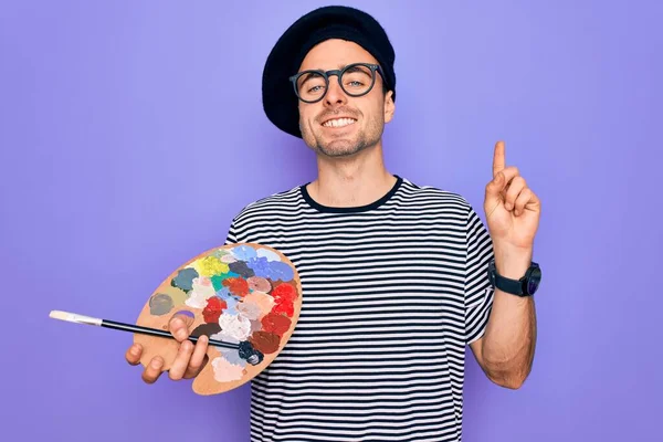 フランスのベレー帽をかぶった青い目の若いアーティストの男と幸せな顔を持つアイデアや質問を指差す指で驚いて絵筆を使用して描画眼鏡 ナンバーワン — ストック写真