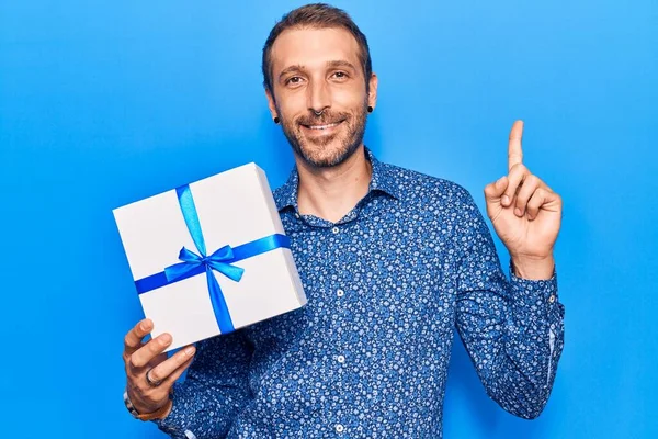 Jovem Homem Bonito Segurando Presente Sorrindo Com Uma Ideia Pergunta — Fotografia de Stock