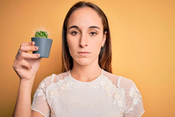 若いです美しいです女性保持小さなサボテン植物ポット上の隔離された黄色の背景とともに自信を持って式上のスマート顔思考深刻な — ストック写真