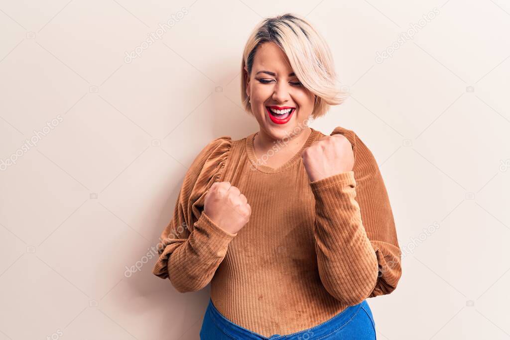 Young beautiful blonde plus size woman wearing casual sweater over isolated white background celebrating surprised and amazed for success with arms raised and eyes closed