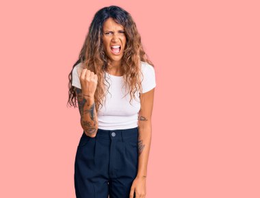 Dövmeli, beyaz tişörtlü, öfkeli ve kızgın genç bir İspanyol kadın öfkeyle bağırırken yumruğunu kaldırıyor. öfke ve agresif konsept. 