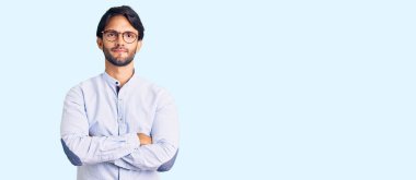 İş gömleği giyen yakışıklı, gözlüklü şüpheci ve gergin, yüzünde çapraz kollu tasvip etmeyen bir ifade. negatif kişi. 