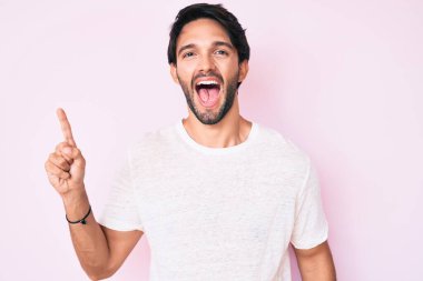 Gündelik beyaz tişört giyen yakışıklı İspanyol adam başarılı bir fikri işaret ediyor. Heyecanlı ve mutlu. Bir numara.. 