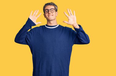 Genç, yakışıklı, günlük kıyafetler ve gözlük takan on numaralı parmaklarıyla onu gösterirken kendinden emin ve mutlu bir şekilde gülümseyen adam.. 