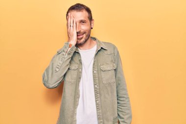 Gündelik kıyafetler giyen genç yakışıklı adam bir gözünü eliyle kapatıyor, yüzünde kendine güvenen bir gülümseme ve şaşırtıcı bir duygu var.. 