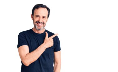 Orta yaşlı, yakışıklı, günlük tişört giyen, neşeli, yüzünde mutlu ve doğal bir ifadeyle, elleri ve parmaklarıyla yüzünü gösteren bir gülümseme olan bir adam. 