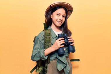 Güzel bir kız çocuğu elinde dürbün tutan kaşif şapkası takıyor. Olumlu ve mutlu görünüyor. Kendine güvenen bir gülümsemeyle dişlerini gösteriyor. 