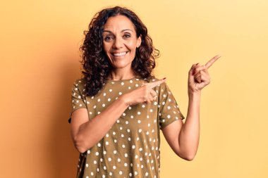 Orta yaşlı, güzel bir kadın, sıradan bir tişört giyiyor gülümsüyor ve kameraya bakıyor. İki eli ve parmağı yana bakıyor.. 