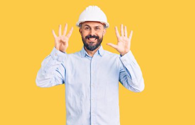 Mimar şapkası takan yakışıklı genç adam dokuz numarayı gösterip işaret ederken kendinden emin ve mutlu bir şekilde gülümsüyor.. 