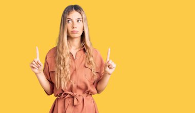 Yazlık tulum giyen güzel beyaz kadın üzgün ve üzgün görünüyor, parmaklarıyla yön gösteriyor, mutsuz ve depresif.. 