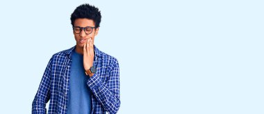 Sıradan kıyafetler giyen ve gözlüklü genç Afro-Amerikan bir adam diş ağrısı ya da diş hastalığından dolayı ağızlarına acı dolu bir ifadeyle dokunuyor. dişçi 