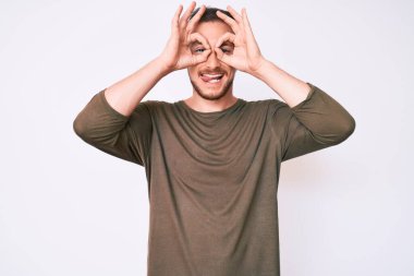 Sıradan kıyafetler giyen genç yakışıklı bir adam dürbün gibi jest yapıyor. Dürbün dilini çıkarıyor, gözler parmaklarından bakıyor. çılgın ifade. 