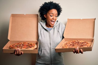 Genç, güzel afro-amerikan afro kadın mutlu ve güvenle gülümsüyor. Yüzünde tebessümle durarak kutular dolusu İtalyan taze pizzasıyla izole beyaz arka planda.