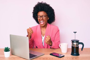 Masada çalışan Afrikalı genç bir Amerikalı kadın bilgisayarını kullanıyor. Şaşırmış ve şaşırmış bir şekilde kollarını kaldırmış ve gözlerini kapatmış bir şekilde kutluyor. 