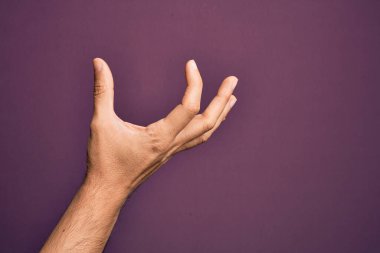 İzole edilmiş mor arka plan üzerinde parmaklarını gösteren beyaz bir adamın eli. Görünmez bir şeyi alıyor, parmakları boşluğu gösteren bir nesneyi tutuyor.