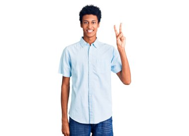 Genç Afro-Amerikalı günlük kıyafetler giymiş iki numarayı gösterip işaret ederken kendinden emin ve mutlu gülümsüyor.. 