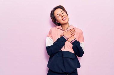 Spor kıyafetleri giyen, elleri göğsünde, gözleri kapalı gülümseyen ve yüzünde minnet ifadesi olan genç bir kadın. sağlık kavramı. 