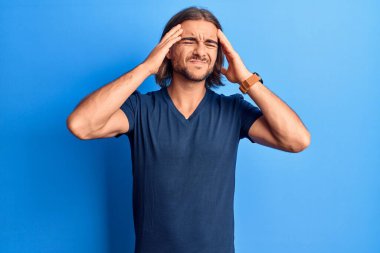 Elleri başının üstünde, günlük kıyafetler giyen genç yakışıklı bir adam. Stres yüzünden başı ağrıyor. migren ağrısı. 