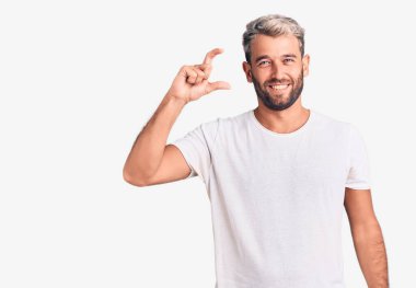 Genç, sarışın, gündelik tişört giyen, el hareketlerini onaylayan, gülümseyen ve başarı için mutlu genç bir adam. kazanan jest. 