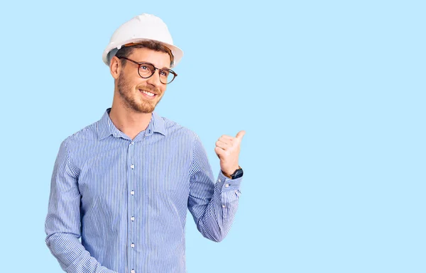 英俊的年轻人 戴着建筑师的硬礼帽 面带微笑 面带微笑 手指头指向旁边 — 图库照片