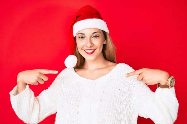 若いですブルネット女性身に着けているクリスマスの帽子を身に着けています自信を持って笑顔で顔 指で自分自身を指す誇りと幸せ — ストック写真