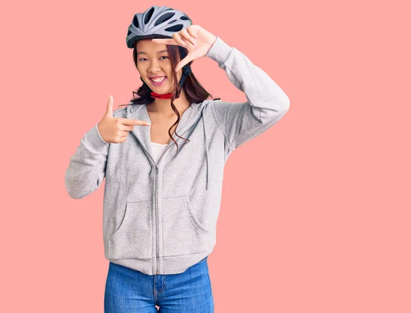 年轻美丽的中国姑娘戴着自行车头盔 面带微笑 手指手画脚 面带笑容 创意与摄影概念 — 图库照片