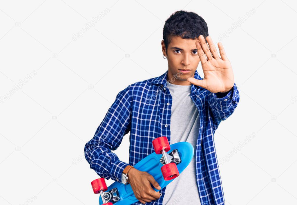 Young african amercian man holding skate with open hand doing stop sign with serious and confident expression, defense gesture 